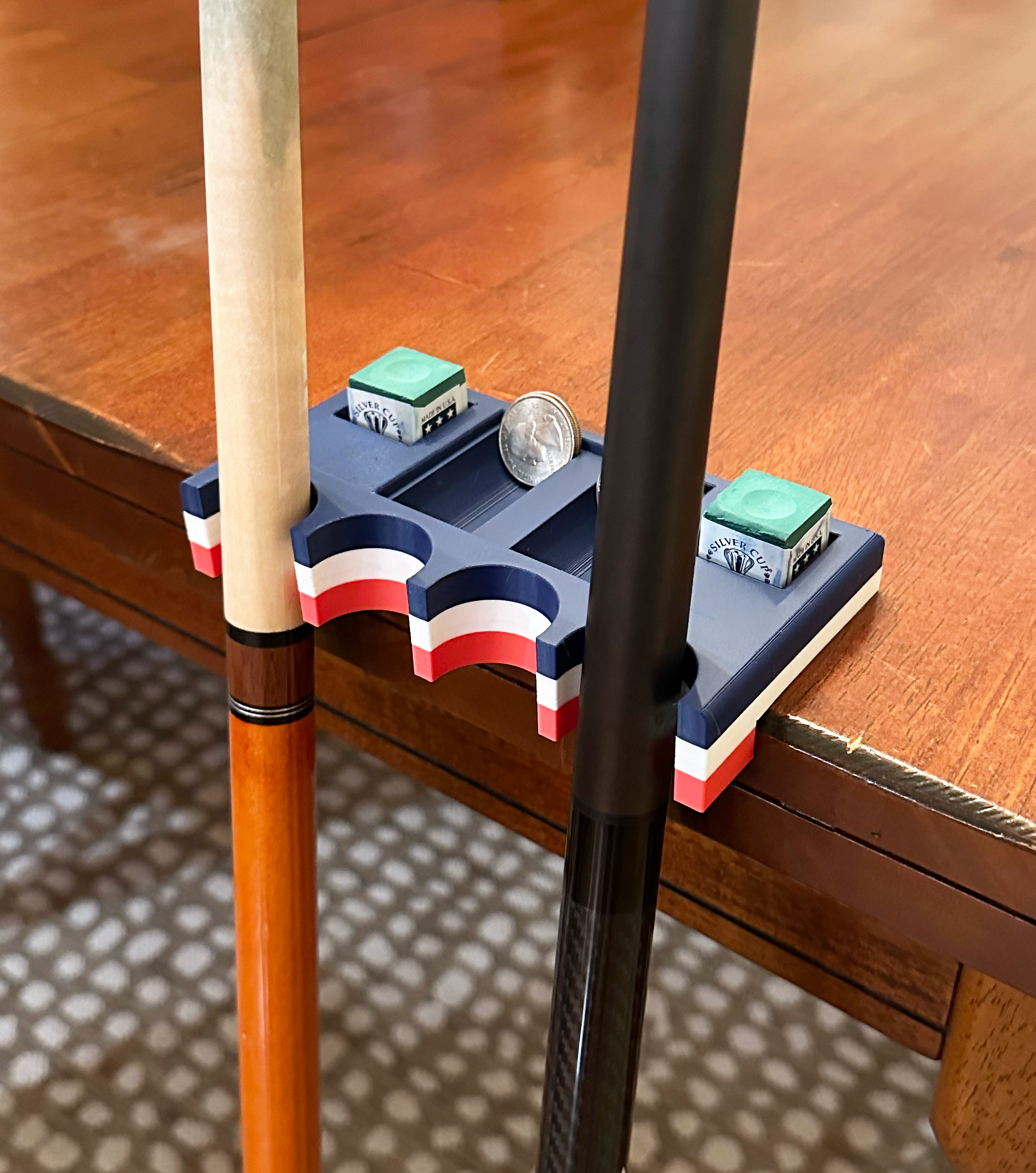 American Flag Pool stick holder on a table with a playing cue and breaking cue holding pool chalk and quarters.